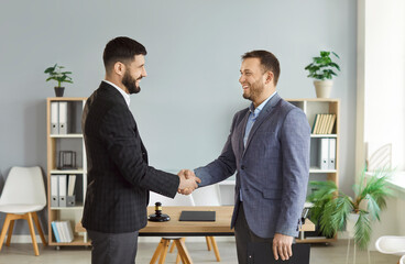 Two smiling men shaking hands in office while celebrating successful legal case. Professional male...