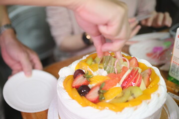 Taipei, Taiwan - November 15th 2025 - Close up view of hand cutting fresh fruit birthday cake with plastic knife.