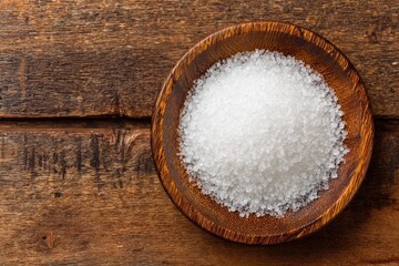 Pile of white salt in wooden bowl on rustic wood