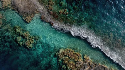 Wandcirkels Koraalriffen Aerial view of turquoise sea around a coral reef with white waves breaking on a rocky shoreline. Concept Turquoise sea, Coral reef, Aerial view, White waves breaking, Rocky shoreline  © Anastasiia