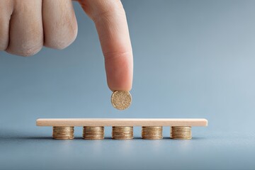 A finger places a coin on top of a balanced structure of coins
