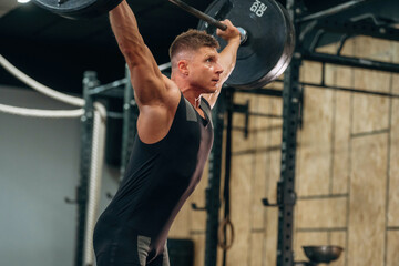 Side view. Athletic man performing weightlifting exercises with a barbell in a gym