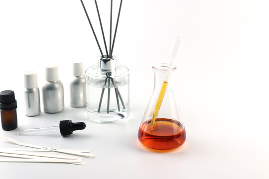 chemical beaker or flask is used on white table with blotting paper fragrance bottle and essential oil bottle are used to blend nice scent for making perfume and reed diffuser by perfumer in lab test