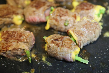 Taipei, Taiwan - November 18th 2025 - Close up view of raw beef rolls wrapped with asparagus and cheese frying in a pan.