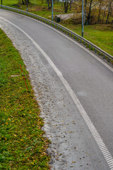 Empty curved wet road bordered by grass on autumn day.