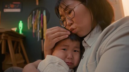 Asian mother holding and comforting her little son in her arms in cozy home, sharing tender, loving, and reassuring family moment - Powered by Adobe
