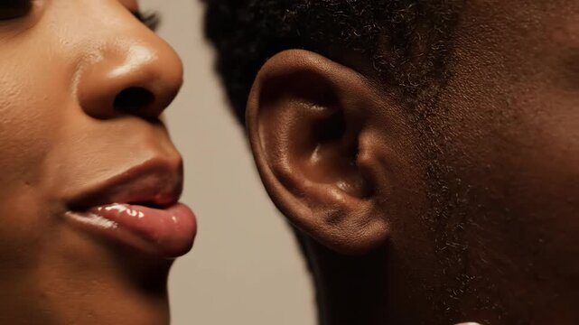 intimate closeup of black woman whispering secret into man's ear. moment of closeness, trust, and private communication. concept of gossip, rumor, or love story.