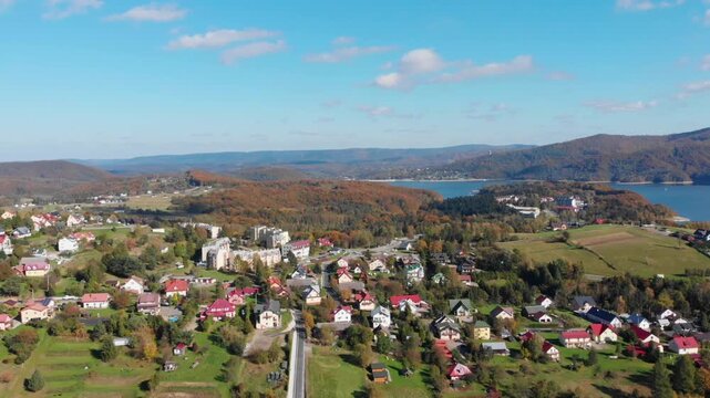 Aerial drone view of Polańczyk village and Solina Lake in Bieszczady Mountains, Poland. Scenic autumn landscape featuring rolling hills and forested shoreline.