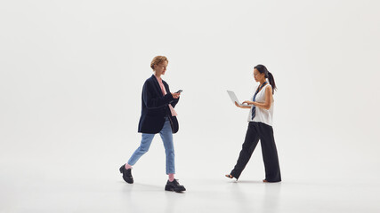 Two young professionals walking and using laptop and smartphone representing digital teamwork. Concept of startup collaboration, mobile productivity, and gender diversity in tech lifestyle.