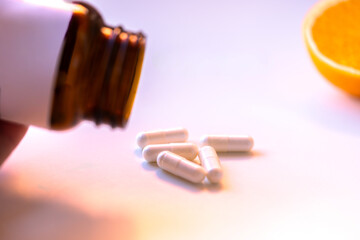 Amber glass bottle with white label and scattered capsules beside a fresh orange half on a white table. Concept of vitamins, immunity, natural supplement and wellness lifestyle.