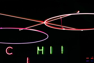 abstract composition featuring bright neon light rings and linear elements in pink, yellow, and white against a dark background. below the installation, green and red illuminated letters add extra dep
