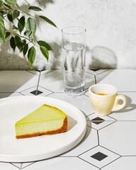 Pistachio cheesecake, a shot of espresso, and water on the table, sunlight.