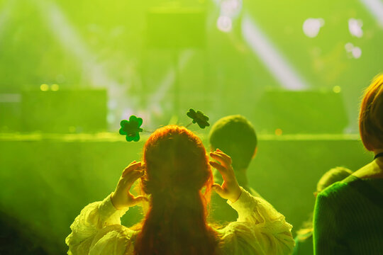 Woman wearing shamrock headband dancing at club party with green lights and Irish vibes. Concept of St. Patrick Day celebration, fun, cultural spirit