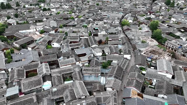 Aerial view of closely packed traditional buildings with gray rooftops, creating a textured urban landscape with narrow streets, Lijiang, Yunnan, China.
