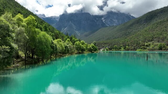 Aerial view of the tranquil turquoise waters meeting lush green hills, and the snow capped Jade Dragon Snow Mountain, Lijiang, Yunnan, China.
