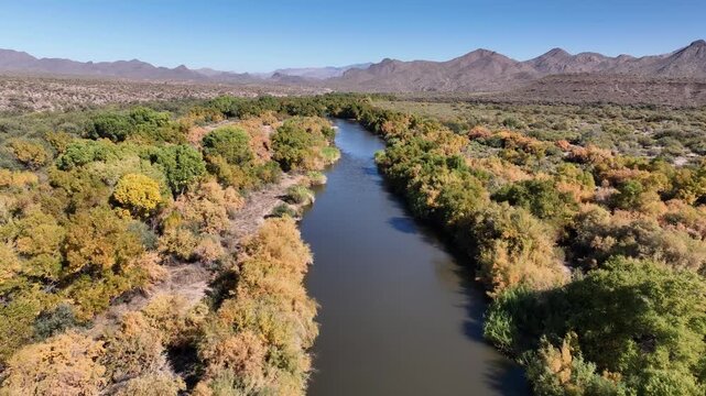 Aerial view of a winding river cutting through the landscape, flanked by trees with mountains visible in the distance, Apache Junction, Arizona, United States.