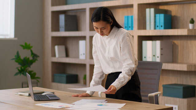 Busy focused Asian Chinese business woman joyful female CEO employer Korean Japanese businesswoman worker analyzing documents report paper searching browsing laptop pc computer software indoor office