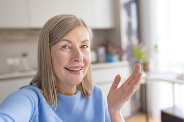Fototapeta premium Senior woman smiling and talking during a video call, communicating with hand gestures from home, showing connection and accessibility for elderly people