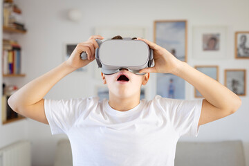 A teenager holds a pair of virtual reality glasses in his hands, looking surprised