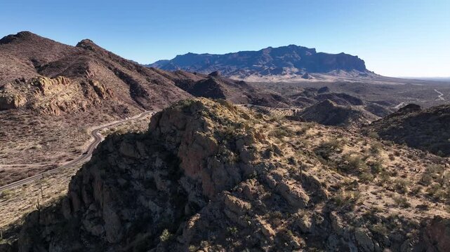 Aerial view of rugged mountains and winding roads creating a stunning contrast between the natural terrain and human infrastructure, Apache Junction, Arizona, United States.