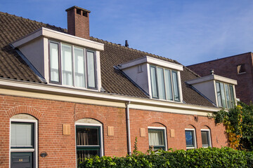 Dormer windows on a traditional brick building with tiled roofs, featuring contrasting red and neutral window frames reflecting autumn trees. High quality photo