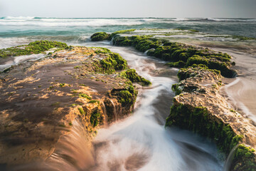 Coastal Serenity Long Exposure Flowing Water Between Rocky Outcrops with Green Algae and Moody Skies Soft Light Captures Coastal Beauty Unveiling Tranquility Smooth Sea Motion