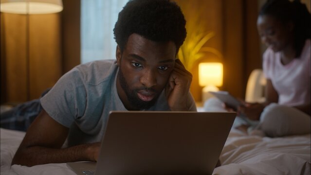 African American family couple weekend evening man boyfriend use laptop watching film lying on bed typing working woman girlfriend using digital tablet relaxing gadget addiction at home bedroom night