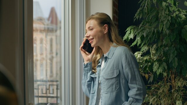 Relaxed woman answer talking mobile phone call looking window at home office Caucasian businesswoman female girl speak smartphone conversation look street waiting delivery taxi ordering discuss work