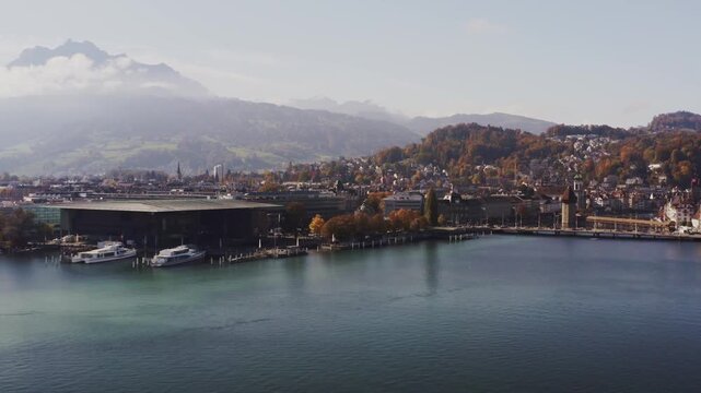 Aerial view of the KKl luzern reflecting on the lake's surface, with boats docked and the city nestled against a backdrop of mountains, lucerne, lucerne, Switzerland.