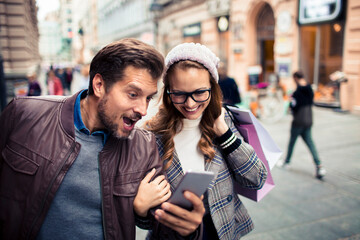 Young adult couple excited, checking smartphone while shopping downtown