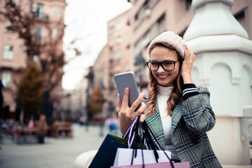 Young woman smiling at smartphone while shopping in city street