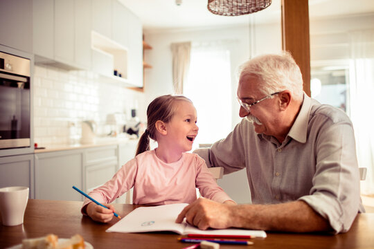 Senior grandfather and child granddaughter laughing while drawing in home kitchen - Powered by Adobe
