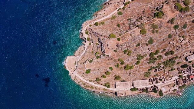 Aerial view of the historic Spinalonga island ruins showing the stark contrast between the arid landscape and the turquoise waters surrounding it, Elounda, lasithi, Greece.