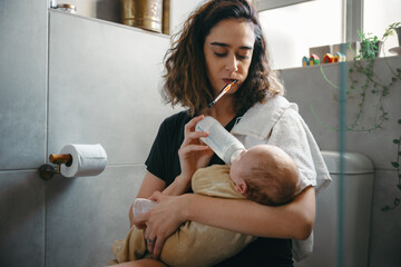 Mother multitasking in bathroom while feeding baby