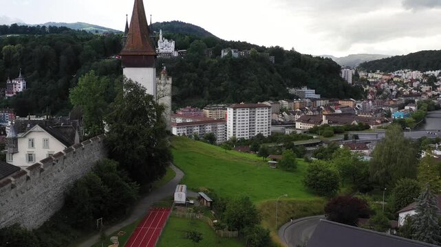 Aerial view of the historic Musegg Wall with its iconic towers, contrasted against the lush green landscape and urban development, lucerne, lucerne, Switzerland.
