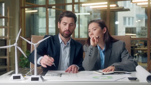 Caucasian Korean business workers environment eco discussion startup working windmills model businessman businesswoman talking green energy wind turbine alternative sources woman man indoors office