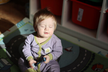 Baby sitting on a colorful play mat indoors, wearing striped pajamas and holding a toy. Bright...