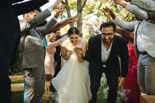 Bride and groom celebrating wedding surrounded by joyful guests under trees
