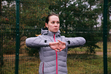 A young woman on a sports field is doing muscle stretching exercises. Warm-up before training. Outdoor training