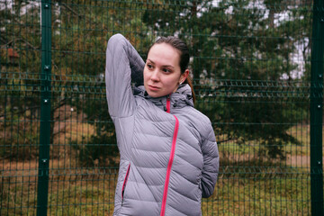 A young woman on a sports field is doing muscle stretching exercises. Warm-up before training. Outdoor training