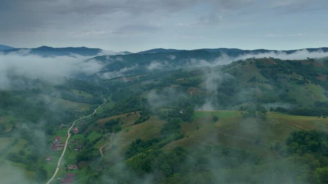 Wide panoramic sweep over misty Transylvanian valley in Romania, drifting morning fog over rolling Carpathian hills and scattered village houses after a summer storm
