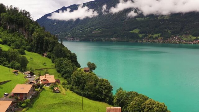 Aerial view of iseltwald village nestled on vibrant green hills meeting a serene, turquoise lake under a cloudy sky, iseltwald, Canton of Bern, Switzerland.