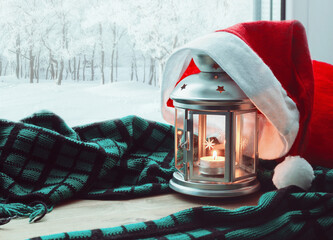Christmas and New Year background, metal silver lantern with candle and Santa hat on the windowsill and winter park outdoor. Concept of Christmas and New Year spending at cozy home