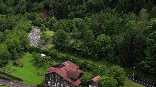 Aerial view of houses nestled amidst verdant trees, with winding roads and a dense forest backdrop, creating a serene landscape, iseltwald, Canton of Bern, Switzerland.