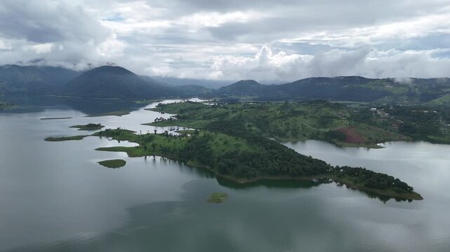 Aerial view of the tranquil Umiam Lake surrounded by lush green hills partially covered in clouds, reflecting the overcast sky, Shillong, Meghalaya, India.