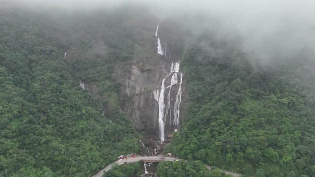 Aerial view of stunning waterfalls cascading down the mountainside amidst dense green trees and misty clouds, Shillong, Meghalaya, India.