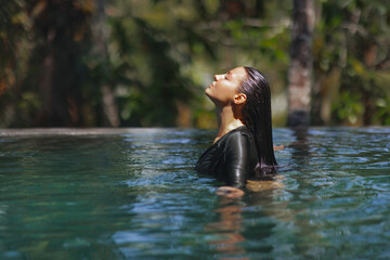 Fototapeta premium Woman Relaxing in Infinity Pool with Eyes Closed Surrounded by Tropical Nature