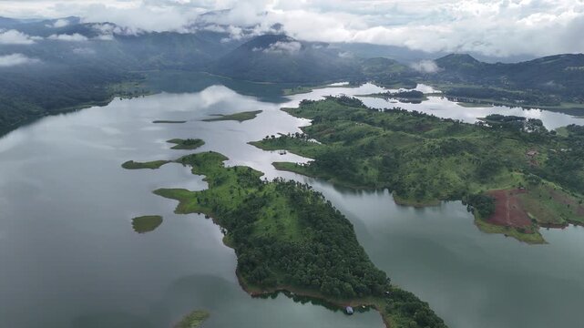 Aerial view of Umiam Lake's serene waters embracing lush green islands under a cloudy sky, creating a mosaic of textures and tones, Shillong, Meghalaya, India.