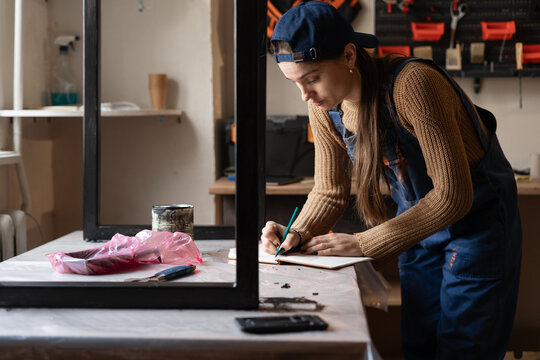 Female handyman writing or checking repair checklist in her repair workshop