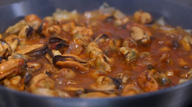 Close view of boiling tomato sauce with mussels, hot bubbles ris ing on surface, intense rich color and lively steam creating warm energetic cooking mood with fresh seafood texture. Mussels with onion